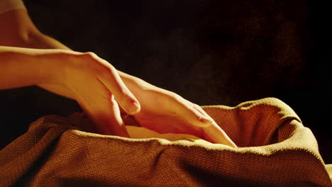 Hands scooping and pouring yellow cornmeal into a burlap sack