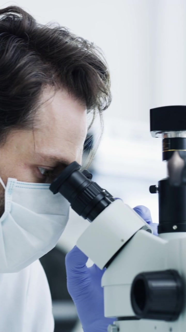 Scientist Wearing Protective Gear Using Microscope in Laboratory