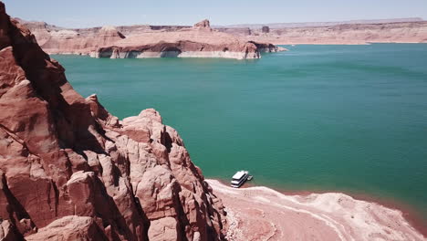 drone shot flying past large red rocks on lake powell to reveal a houseboat and the lake