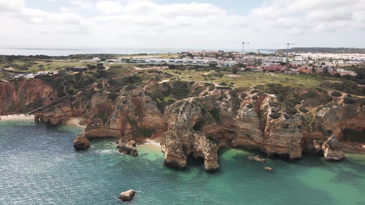 Aerial drone flies left focusing on dramatic rock formation, turquoise sea, and cliffs in Lagos Algarve