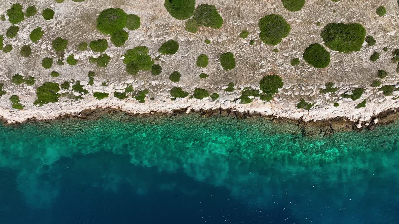 Aerial top down pan across rocky coastal green shrubs and shimmering turquoise waters, Kornati National Park, Croatia