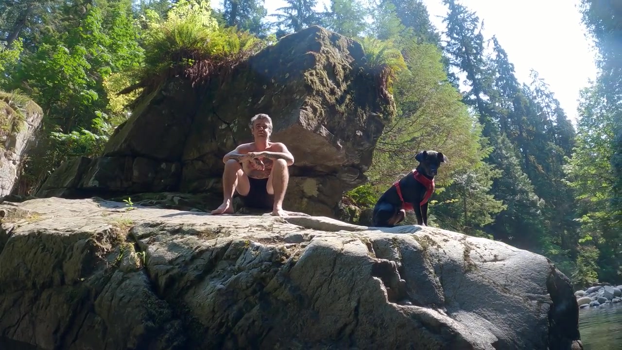 A man and his dog sit on a large rock boulder in Inter River Canyon in North Vancouver, British Columbia, Canada