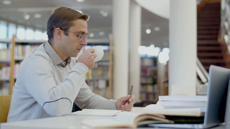 Mand drikker te, mens han studerer på biblioteket.