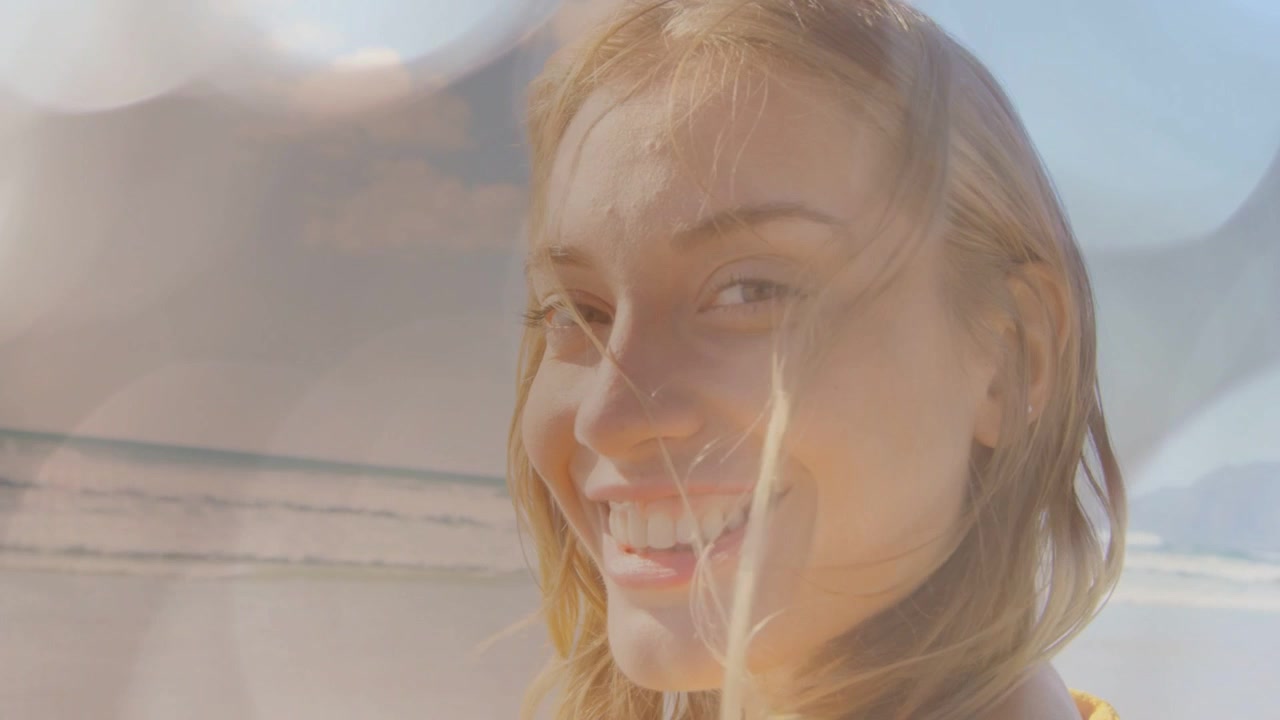 Kvinne som snur seg mot kamera mens det zoomes inn og vinden blåser i håret, linseglimt fremhever smilet for reise