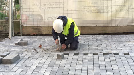 public ajuntament de barcelona worker with hammer, helmet and yellow jacket hammering a square block of concrete on under construction pedestrian street or sidewalk