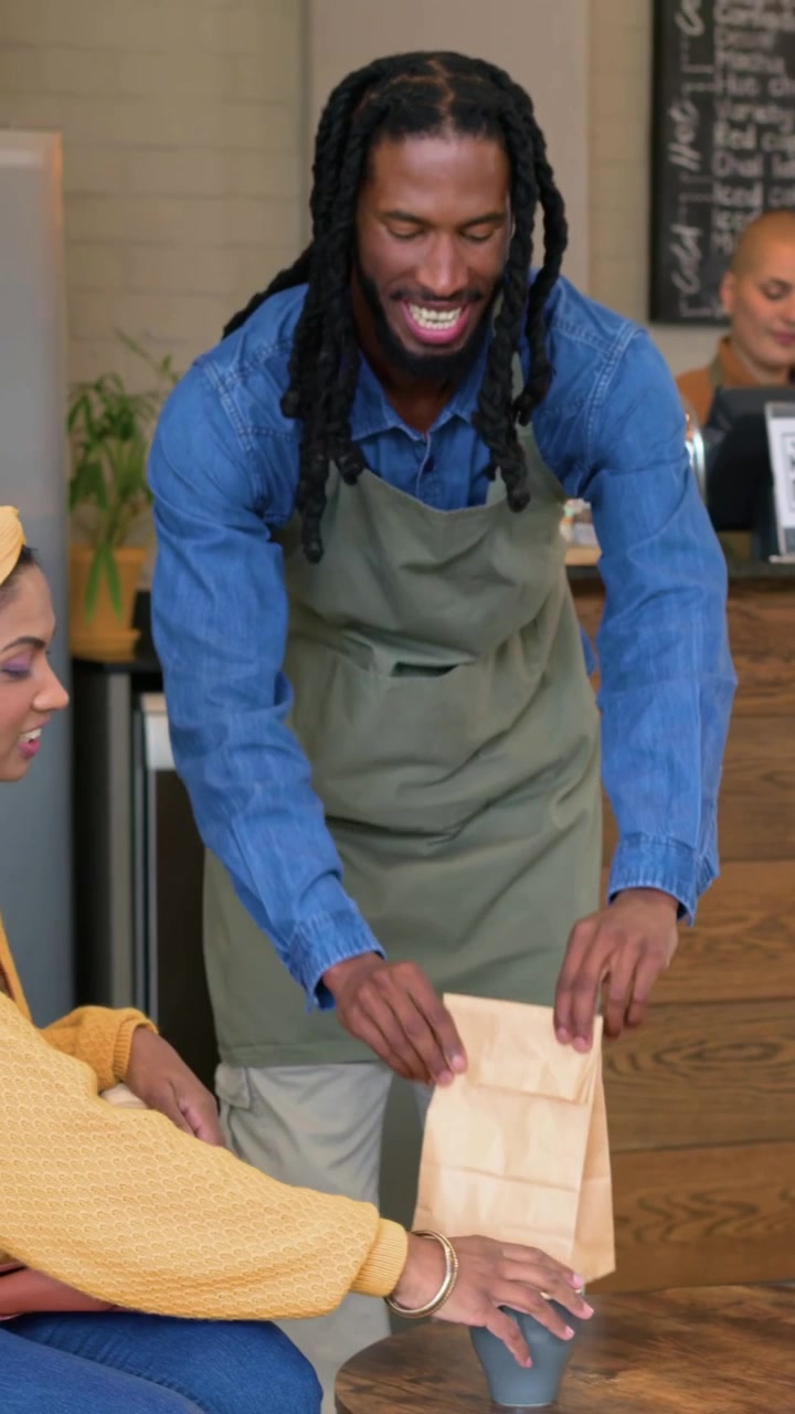 Video verticale: Barista con grembiule si muove dopo un avviso dal POS al caffè, posizionando una tazza e un sacchetto di carta.