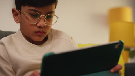 close up of young boy sitting on sofa at home playing games or streaming onto digital tablet 4