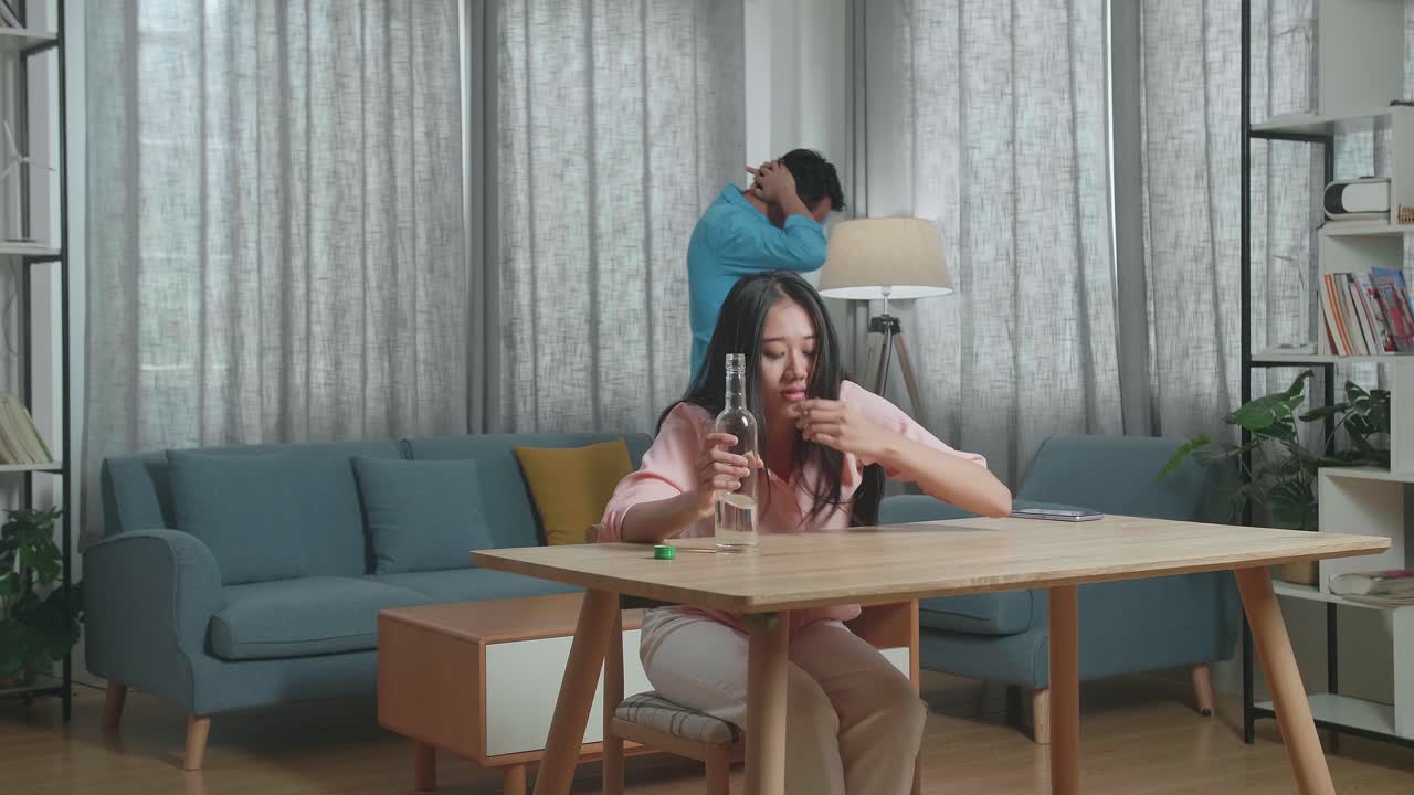 술에 취한, 우울한 아시아 여성이 술을 마시기 전에 글라스에 보드카를 부어주고 집에서 그녀의 뒤를 따라 는 남자