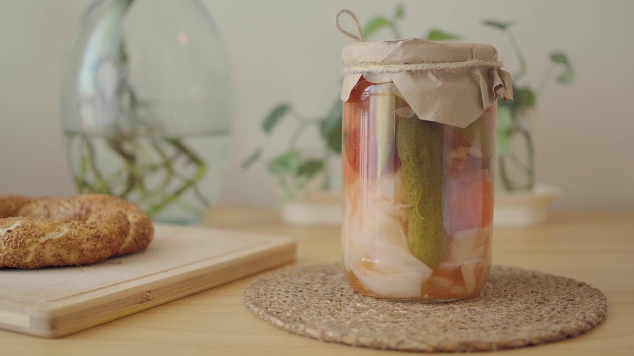Hand Picking Up a Jar of Pickled Vegetables from a Wooden Table