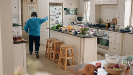 happy teenage boy with down syndrome dancing in kitchen having fun celebrating listening to music wearing headphones enjoying weekend