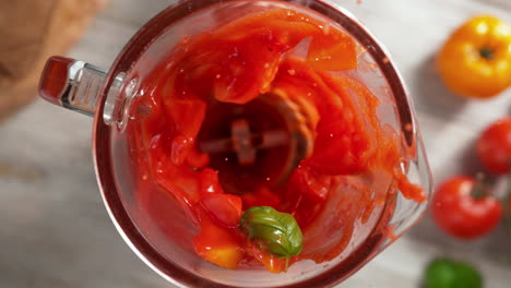 batido de tomate con hoja de albahaca mezclado en una licuadora de vidrio en cámara lenta, vista de arriba, dentro del dispositivo