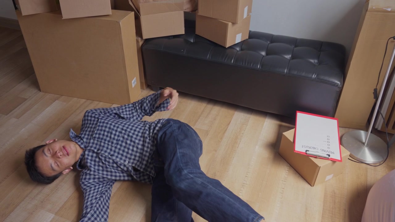 Exhausted young man collapses and lies down on floor to rest after finishing of moving into new home
