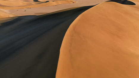 aerial view low over sunlit sand dunes in the namib desert, sunset in namibia