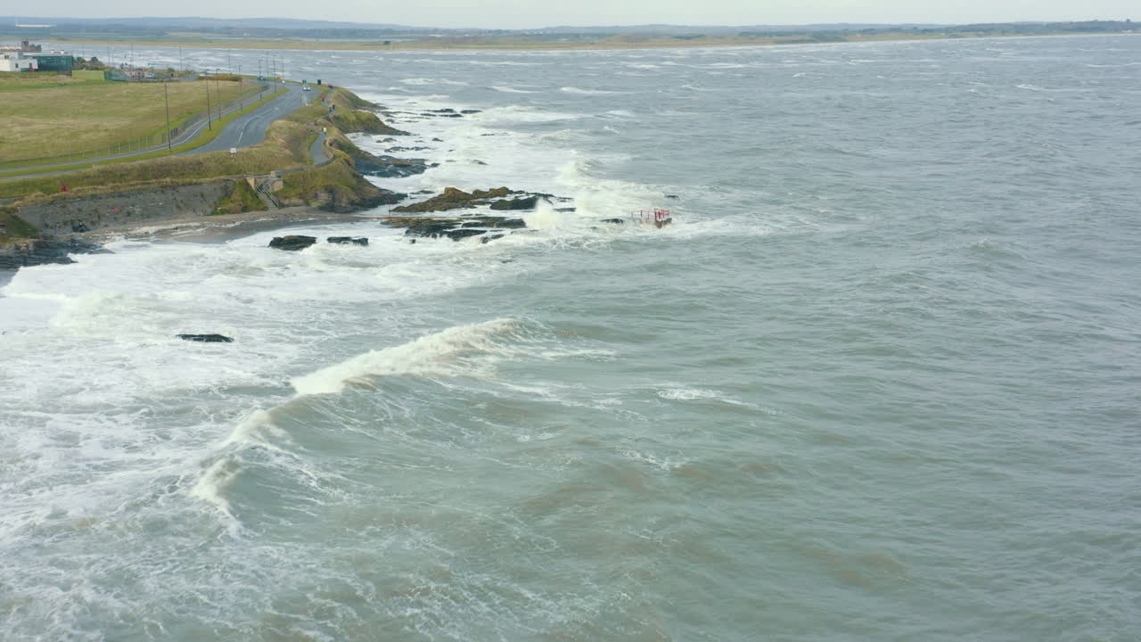 vista aérea de las olas rompiendo contra las rocas a lo largo de la costa durante una tormenta