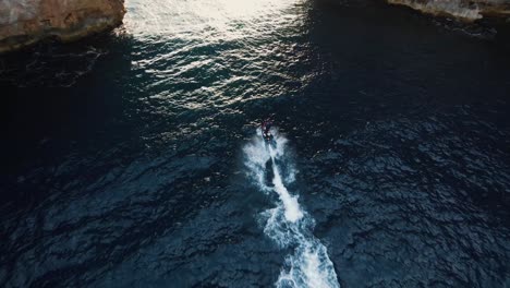 aerial view of an electric surfer going fast and passing under a rocky archway