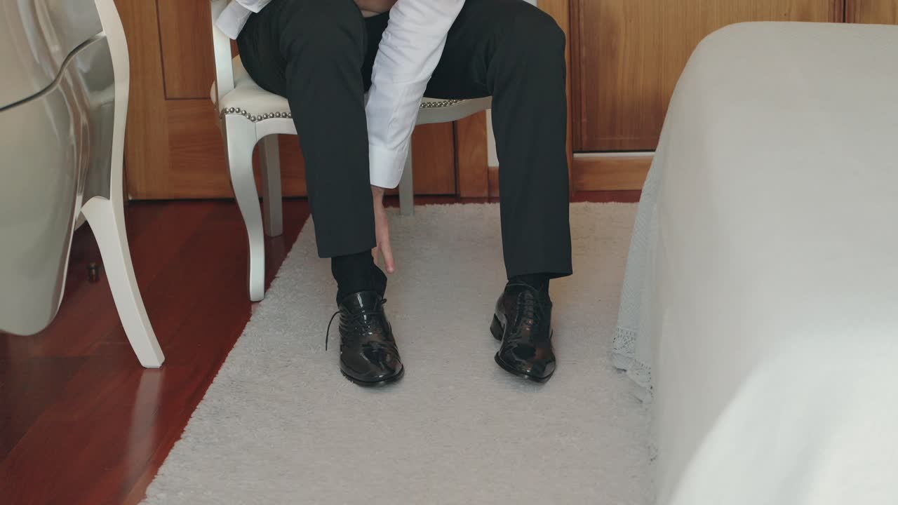 Primo piano di un uomo che si allaccia le scarpe seduto su una sedia con pantaloni neri e scarpe eleganti