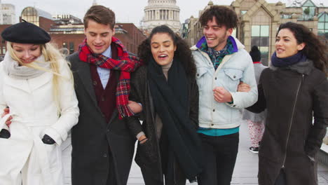 group of young friends walking over millennium bridge in london