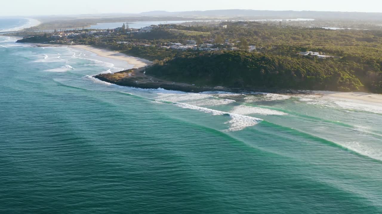 Veduta aerea con drone delle Falesias de Morro Branco che mostra la costa sinuosa, la spiaggia sabbiosa, le onde dell'oceano, l'acqua blu-verde e il paesaggio costiero alla luce del giorno.