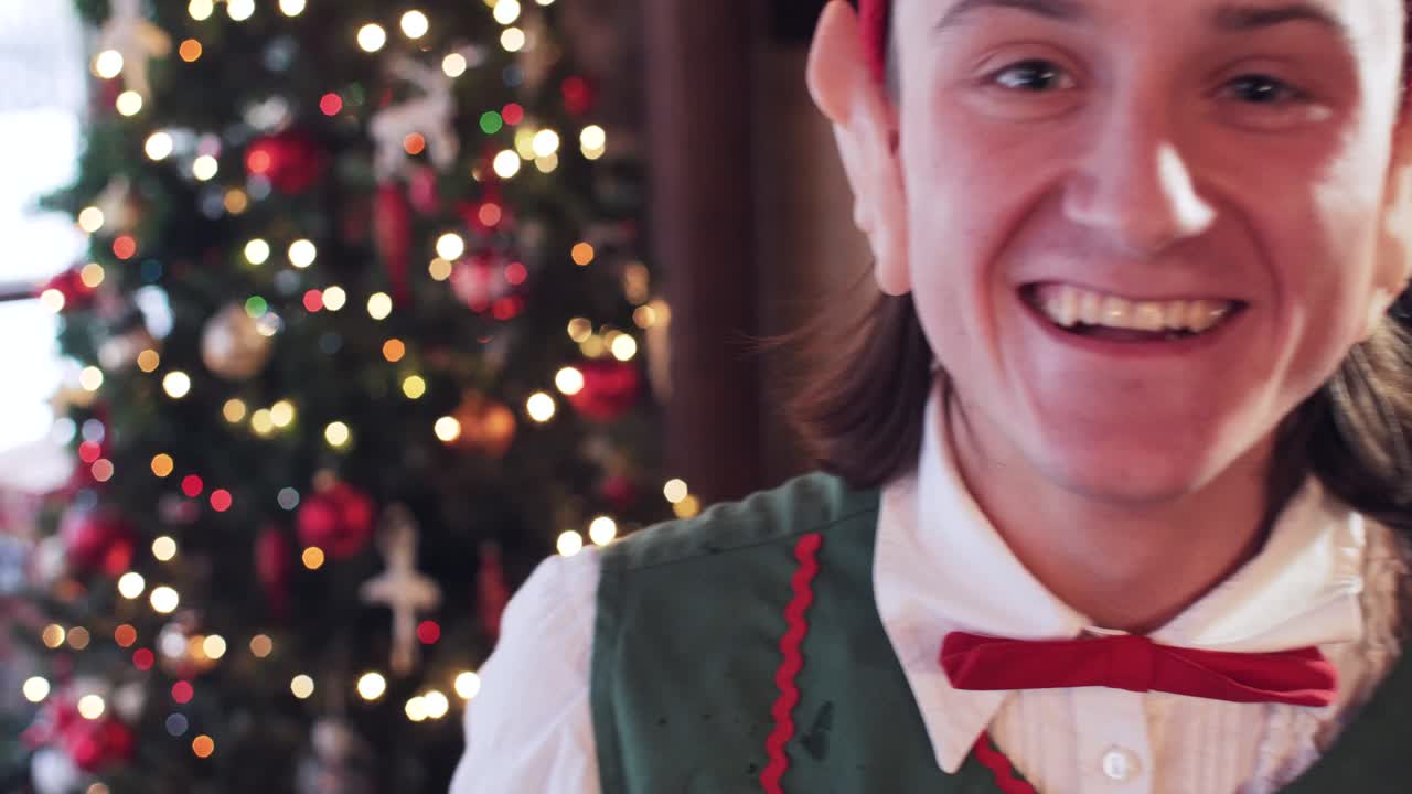 The elf in the santa claus residence is fooling around and having fun with a magnifying glass. New Year tree in the background