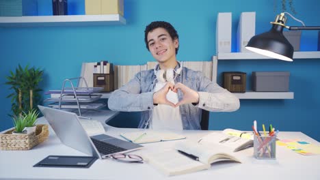 happy male student is making hearts with his hands, smiling towards the camera.