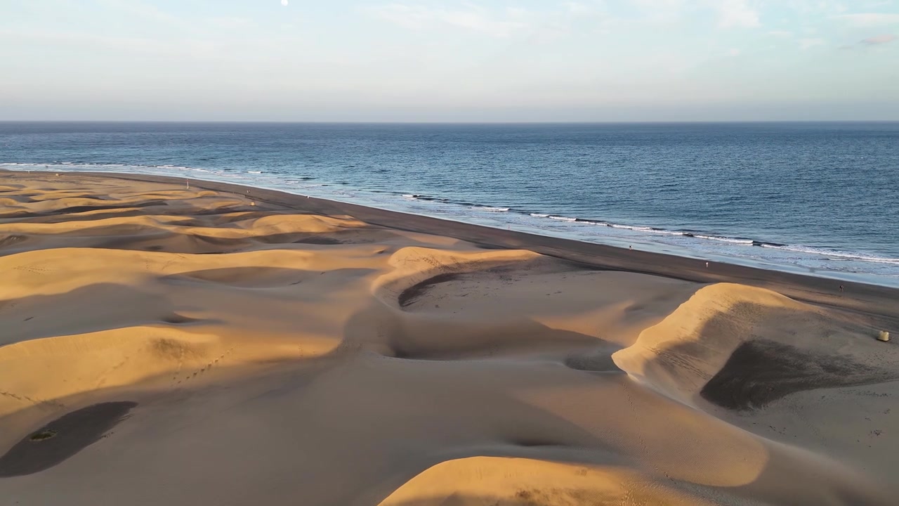 Maspalomas dunes meet the Atlantic shoreline in warm light on Gran Canaria, aerial