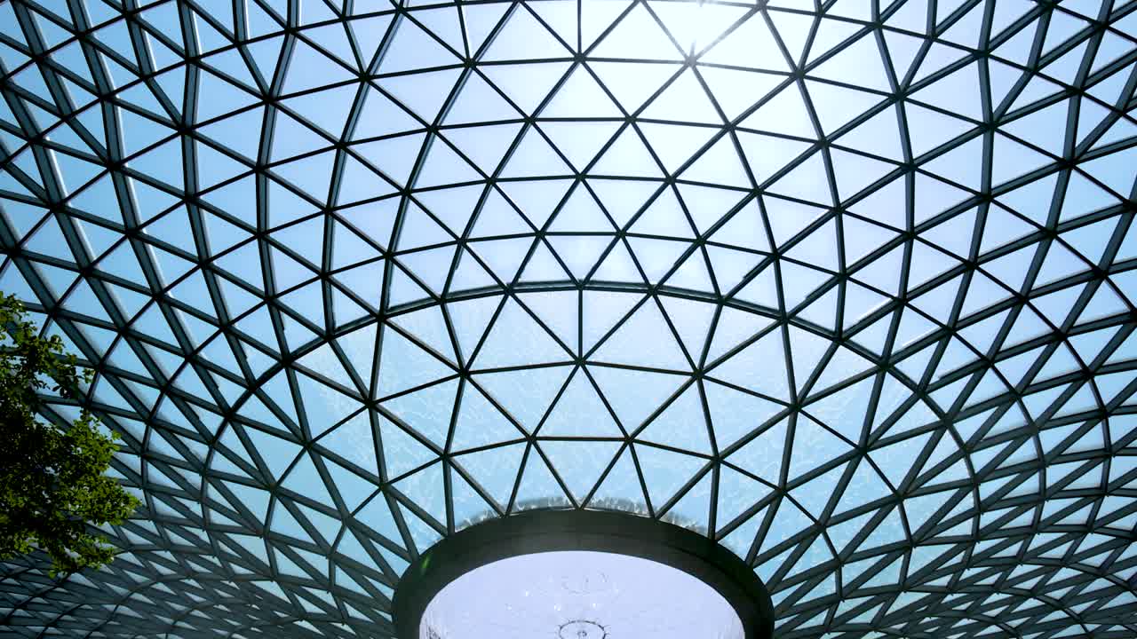 Camera tilts upward from lush indoor waterfall to expansive geometric glass dome ceiling, capturing natural light and architectural details in a modern indoor garden