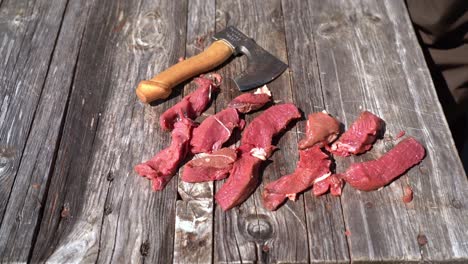 sharp small hiking axe thrown down at table besides sliced raw deer meat in slow motion - outdoor food preparation and survival