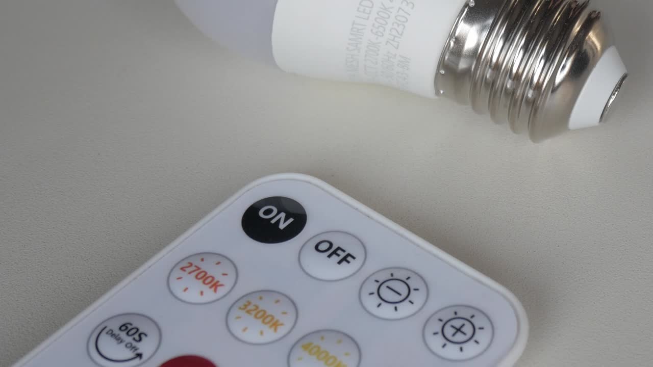 Close-up of smart LED bulb and remote control on white background, pan right