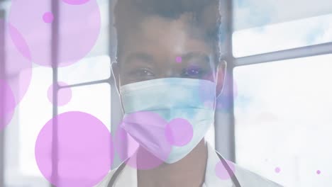 Animation-of-floating-pink-dots-over-happy-african-american-female-doctor-in-face-mask