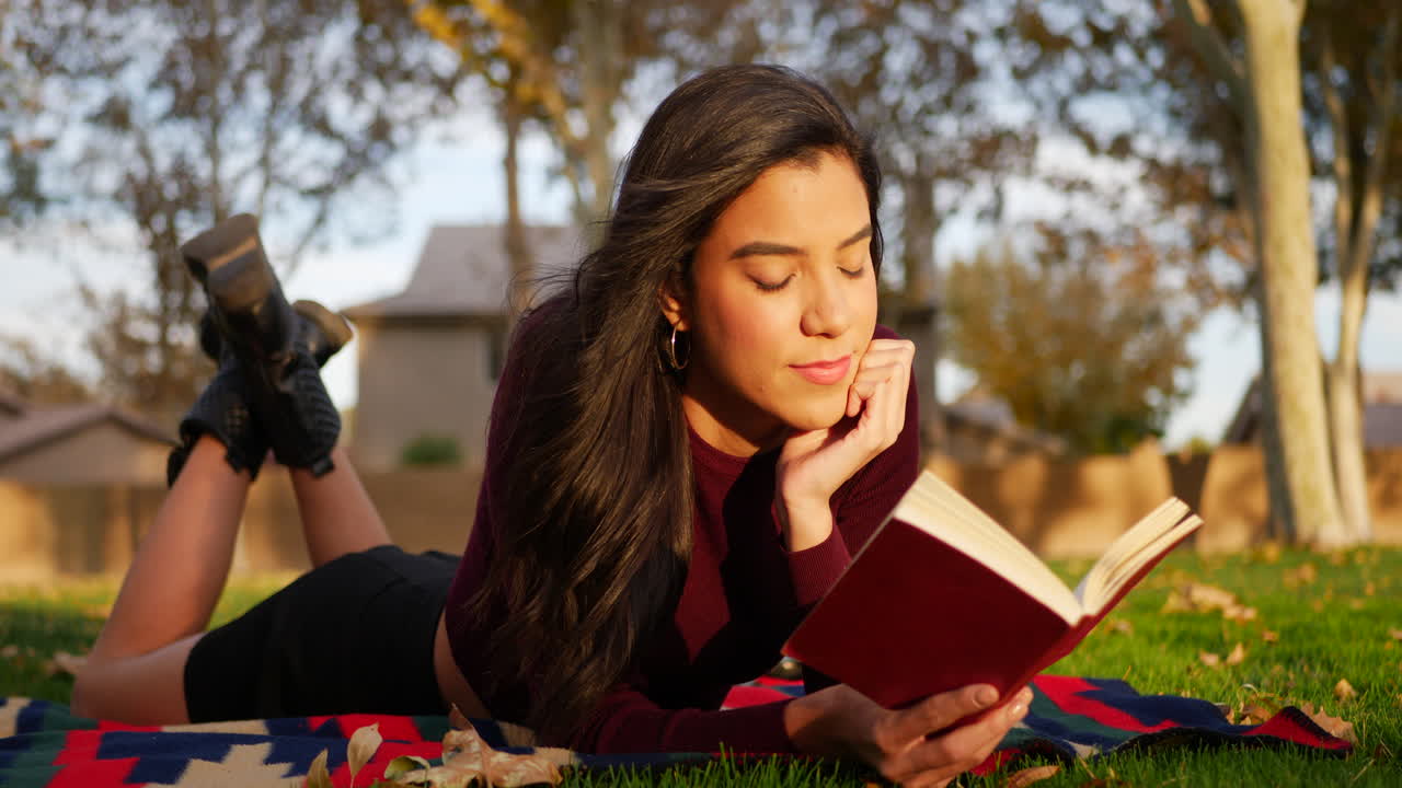 A young hispanic school girl reading a book and studying in the park before her college literature class