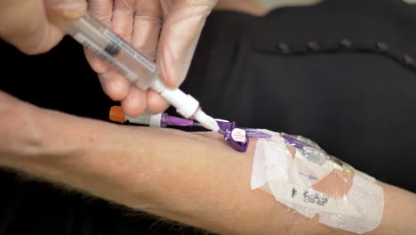 toma vertical de una enfermera médica que realiza una visita a un paciente intravenoso en casa usando guantes estériles e inyectando solución salina en el torrente sanguíneo a través de una línea picc