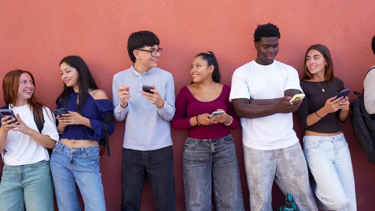 Gruppo eterogeneo di giovani che usano smartphone davanti a un muro rosso