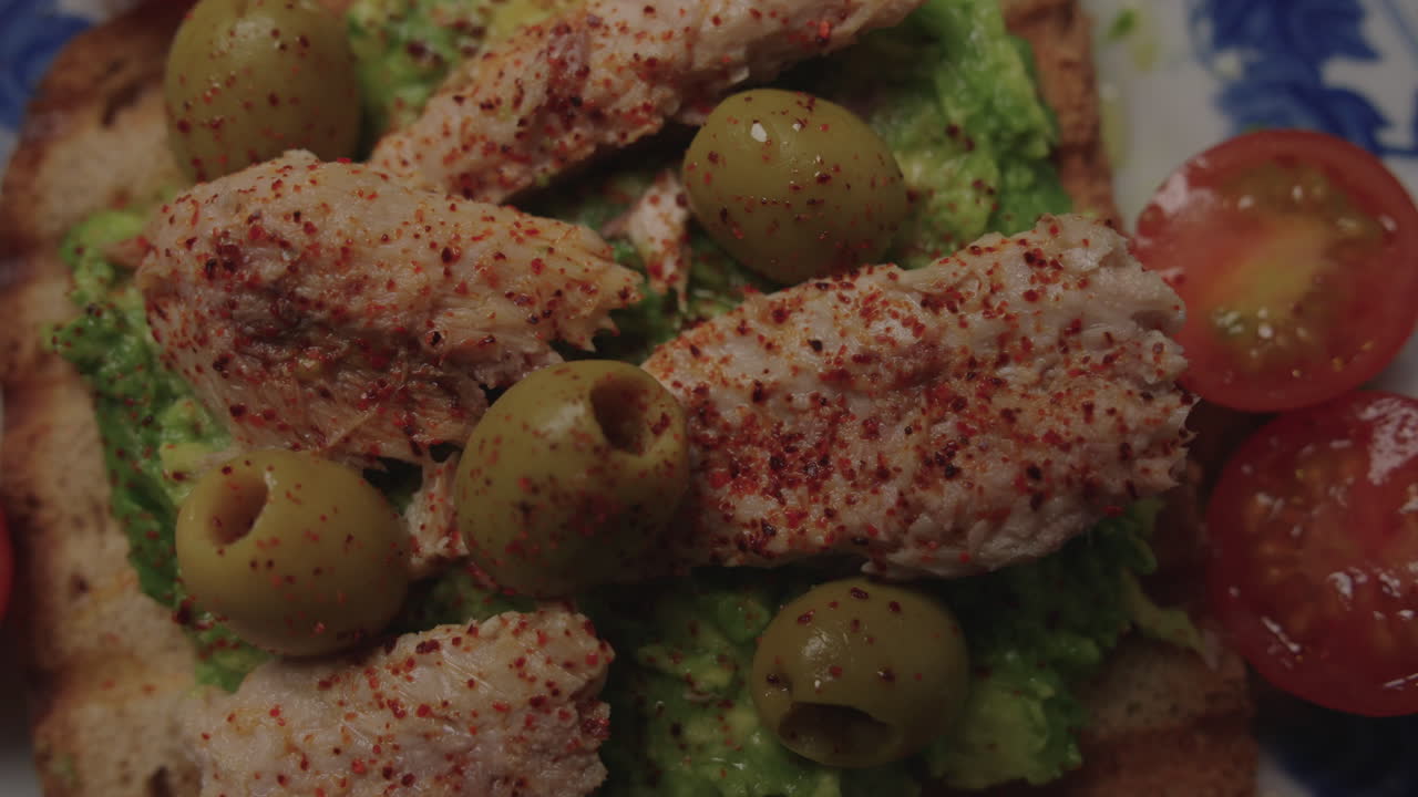 Primo piano dettagliato di toast con avocado e tonno, olive verdi e pomodorini che mostrano la consistenza e la freschezza