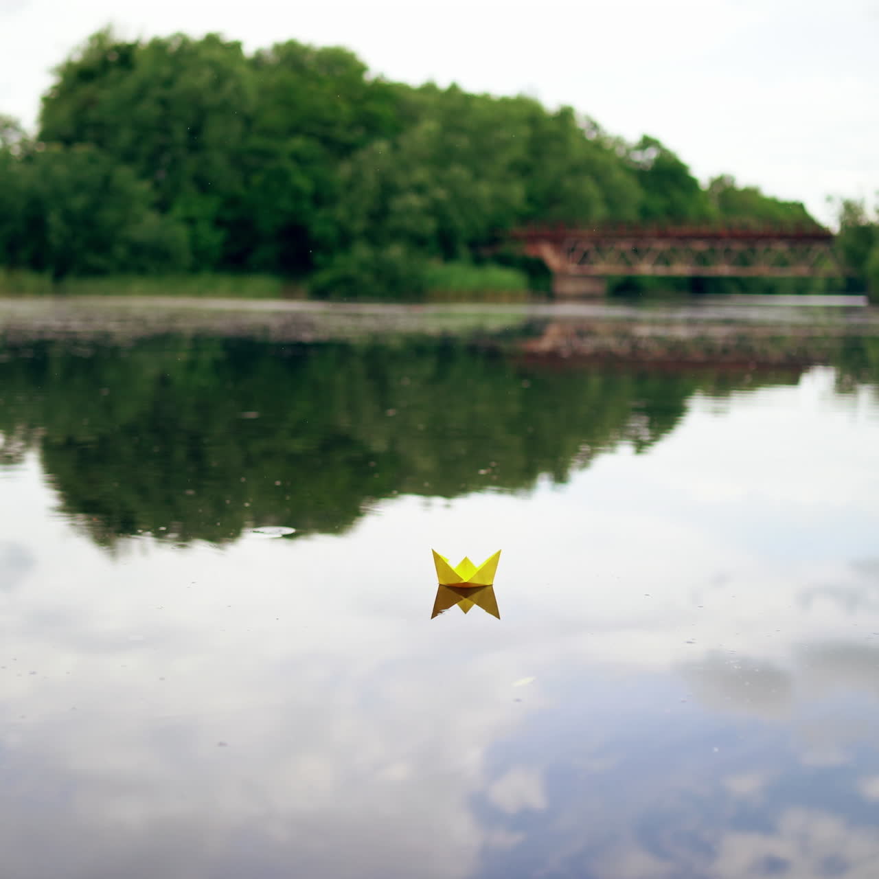 Handmade yellow and blue paper ships are floating on the river in the evening. Two origami boats are sailing on calm river with a little rain falling from the sky into the water.
