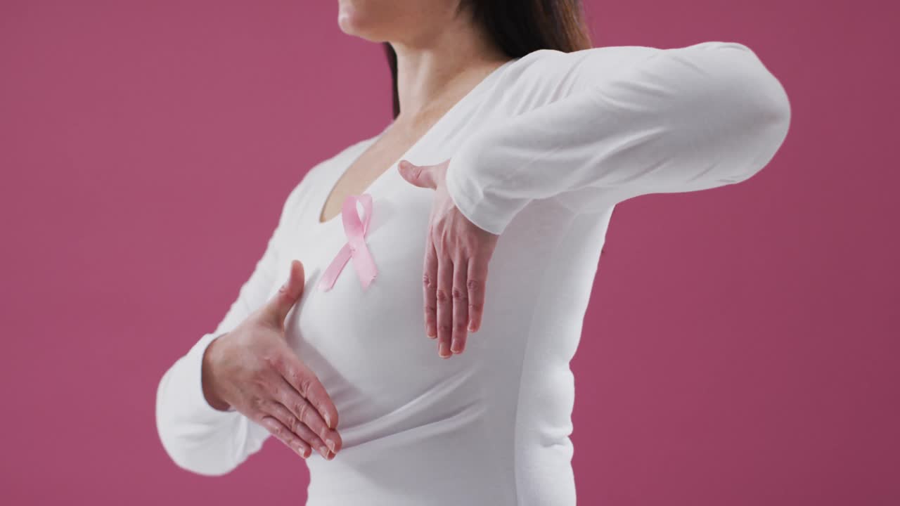 Parte centrale del corpo di una donna che mostra il fiocco rosa sul petto su sfondo rosa