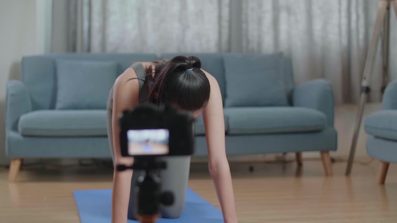 joven entrenadora asiática mujer en ropa deportiva hablando a la cámara y estirándose mientras graba ejercicios de enseñanza en casa