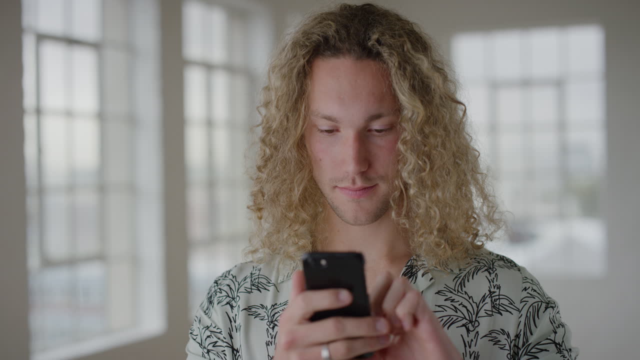 portrait of attractive young man student using smartphone texting browsing online social media reading messaging on mobile phone technology in apartment
