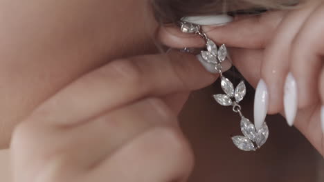 Woman-with-white-manicure-puts-silver-floral-style-earring