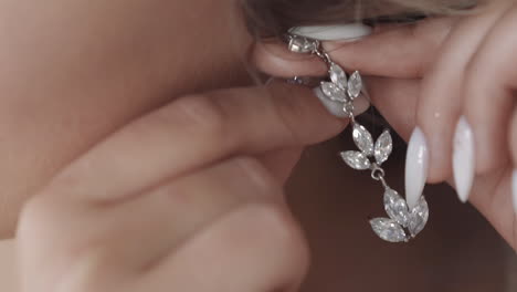 woman with white manicure puts silver floral style earring