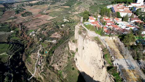 Clip-De-Drones-Moviéndose-Lentamente-Hacia-Edificios-De-Terracota-En-La-Cima-De-Un-Acantilado-Rocoso,-Con-Tierras-Agrícolas-En-Las-Laderas-De-Abajo,-En-Ronda,-España