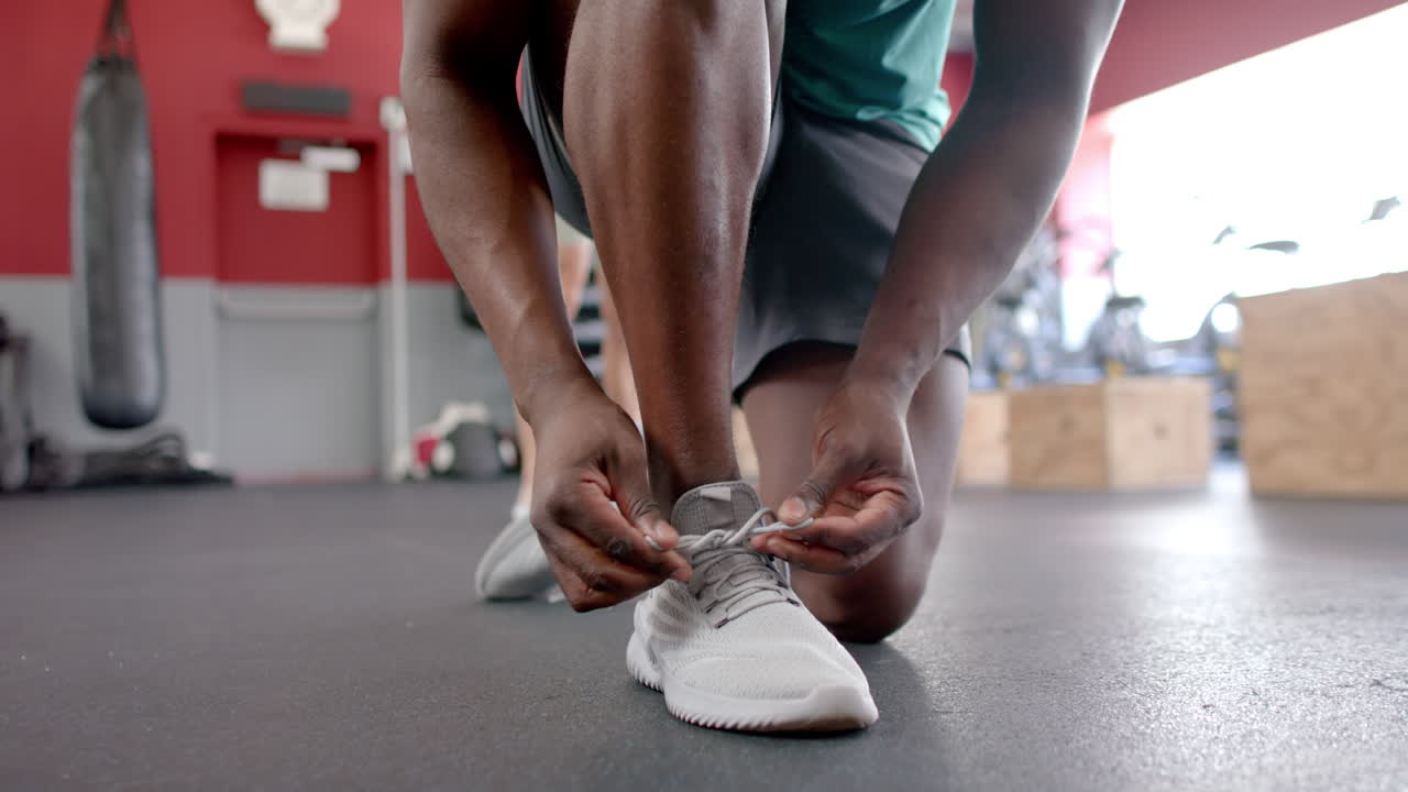 Uomo afroamericano allaccia le sue scarpe da ginnastica in palestra.