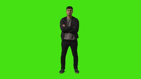 full length shot of fed up casually dressed young man standing against green screen folding arms and putting hands in pockets