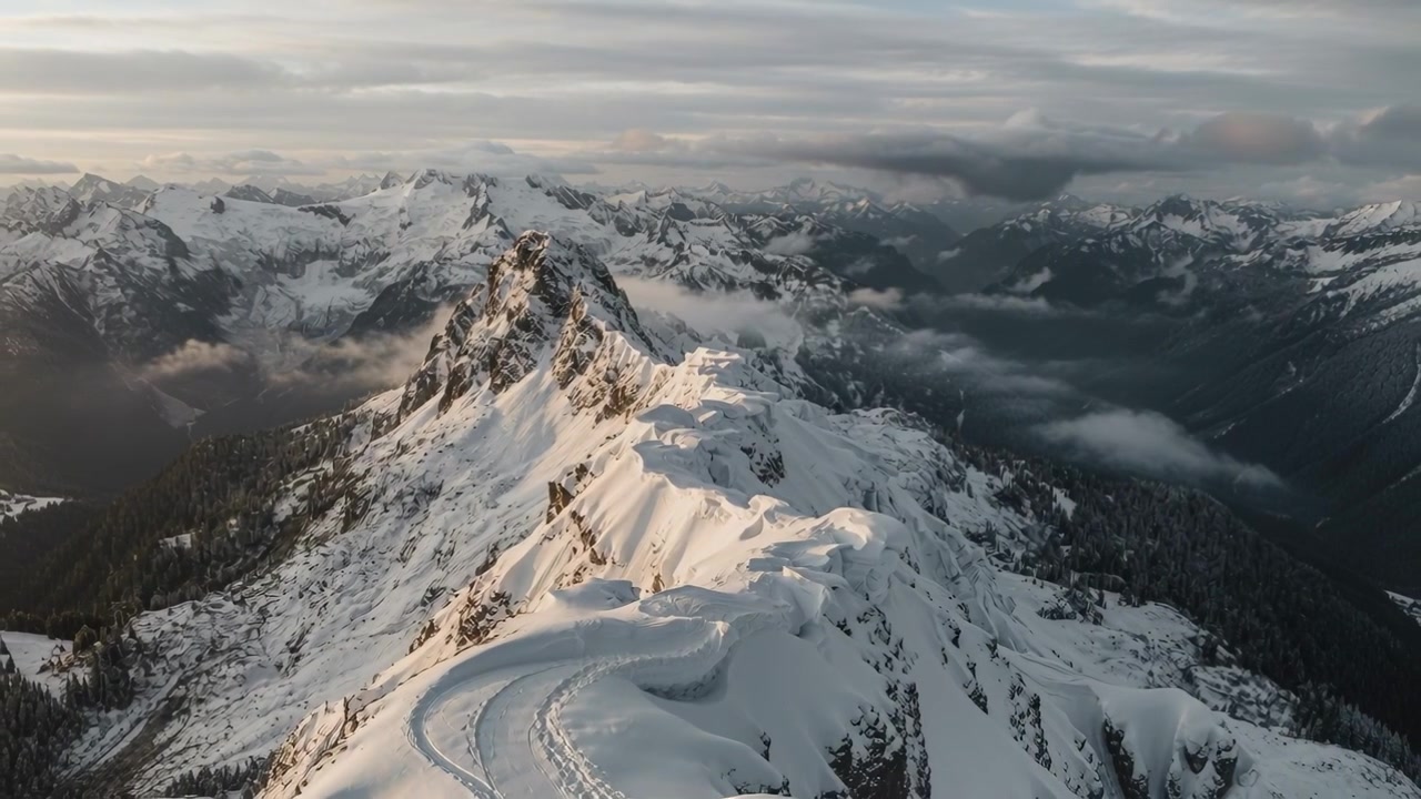 Drone che decolla rivelando una cresta montuosa innevata durante un sorvolo, mostrando un sentiero tortuoso.