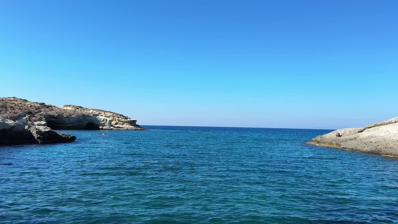Sotto un cielo azzurro brillante, le onde scintillano sotto il sole estivo al largo della costa di Milos, Grecia