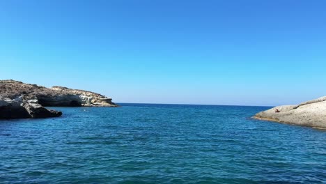 under a bright blue sky, waves sparkle in the summer sun off the coast of milos, greece.