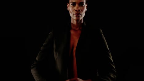 androgynous man in blazer posing against black background