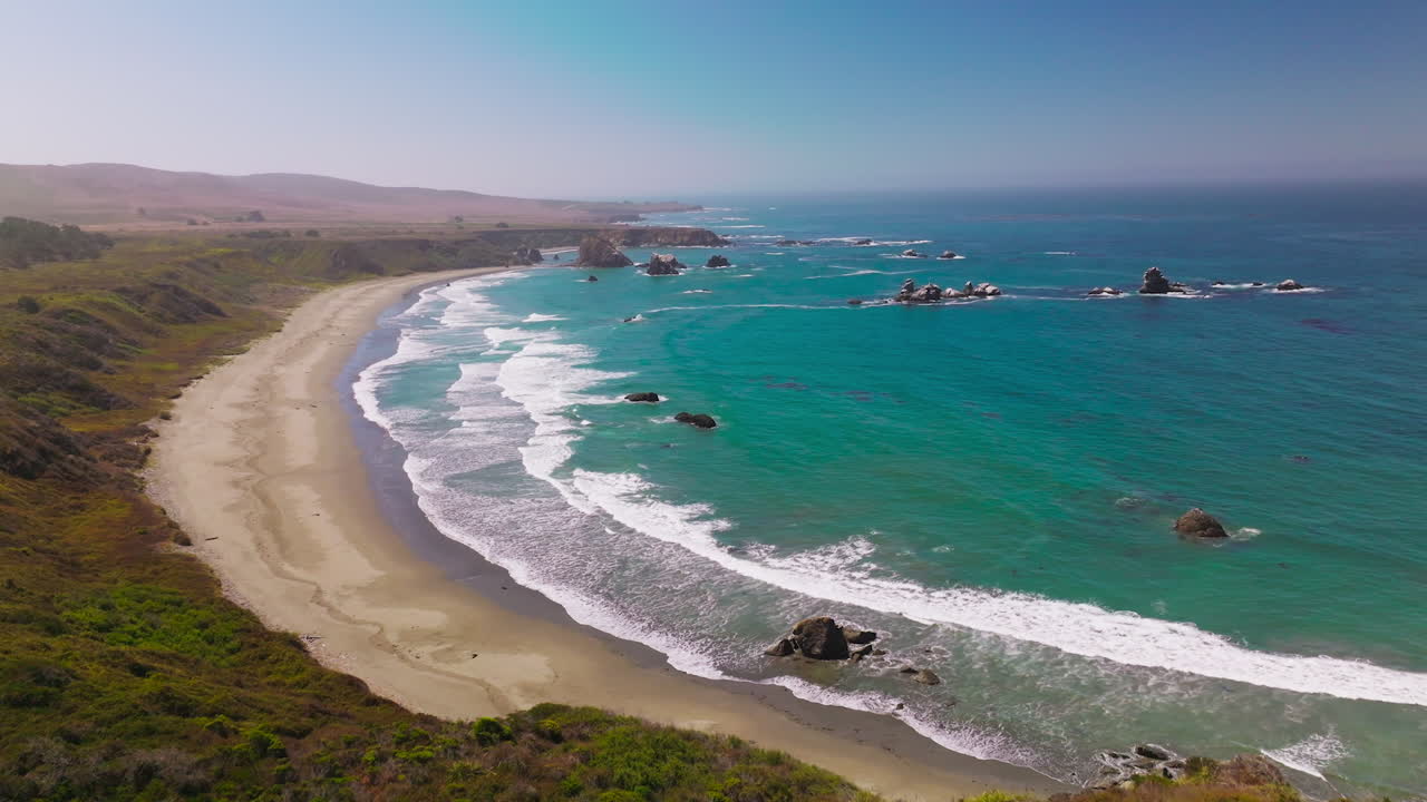 Beautiful hypnotizing foamy waves arriving to the sandy beach. Rocky shore covered with grass. Some stones peeping from water. Aerial view.