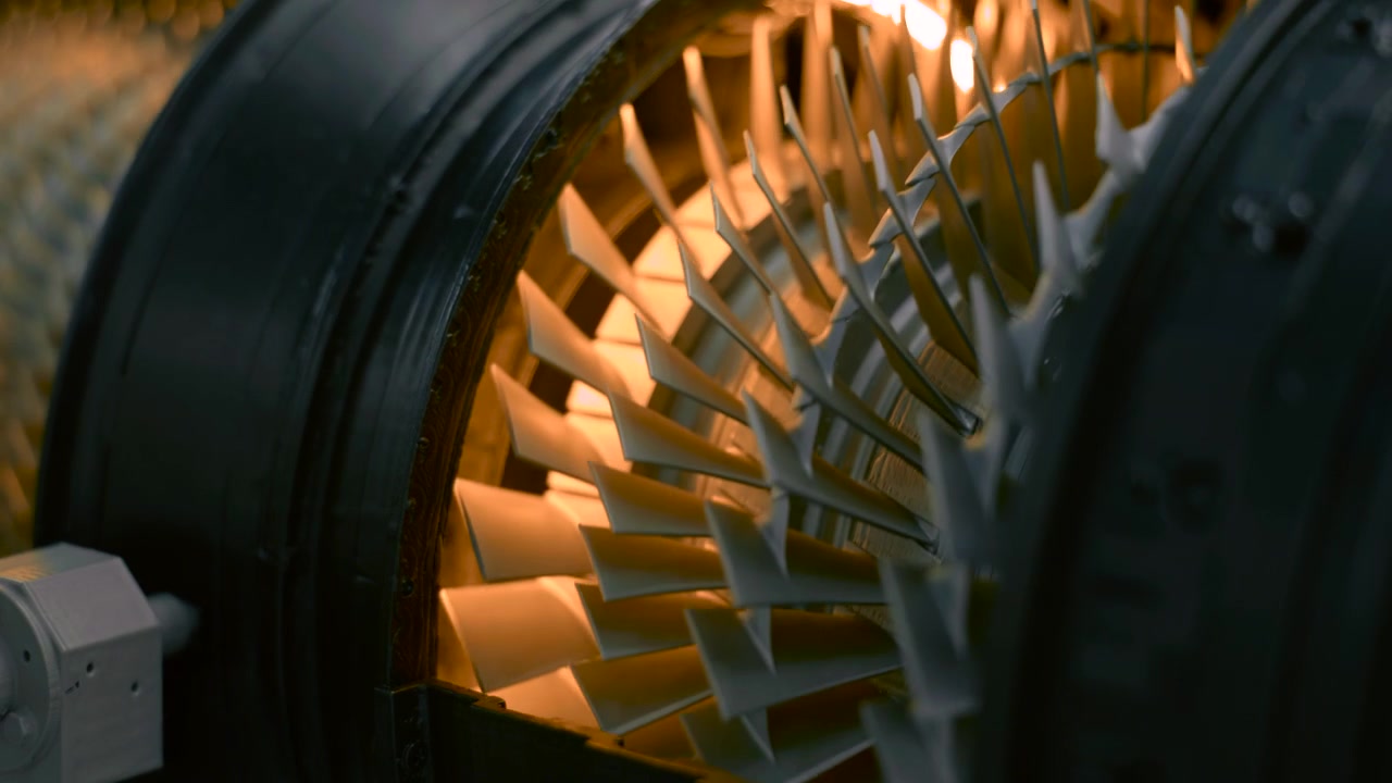 Vue rapprochée en contre-plongée de la chambre interne d'une turbine axiale, montrant un carter circulaire, des aubes métalliques inclinées, des détails de précision, un éclairage orange chaud, une texture industrielle et une structure mécanique conçue