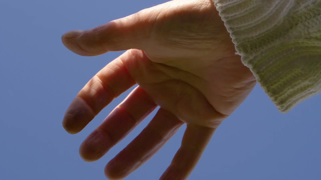 Single hand reaching out against clear blue sky medium shot
