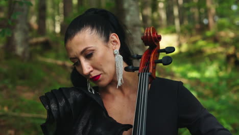 Woman with cello in the forest. Portrait of a dark-haired woman playing the musical instrument on green nature background. Close-up.